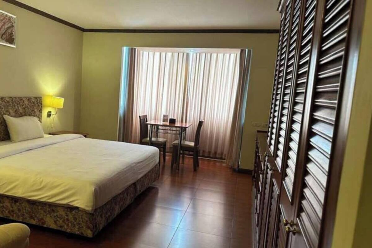 A hotel room with a bed, bedside tables, a desk with chairs, a window with curtains, and a wardrobe.