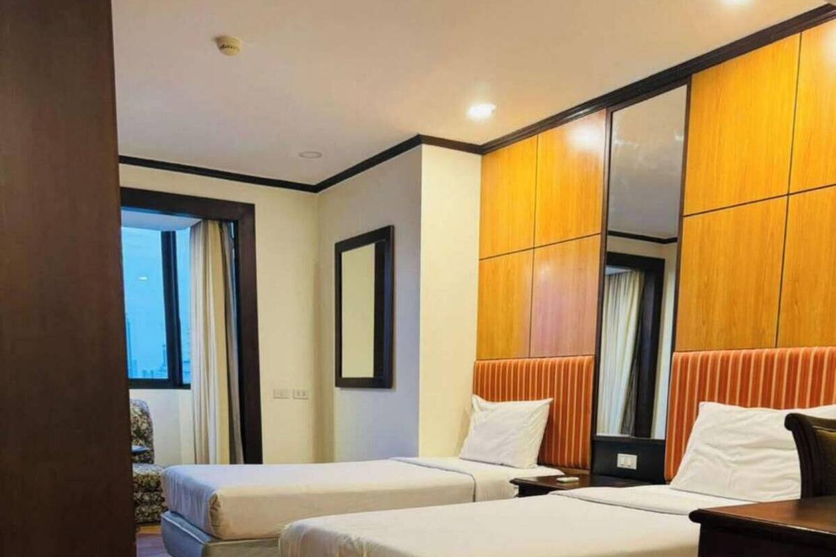 A hotel room with two beds, a large mirror, wooden flooring, and a view of the city.