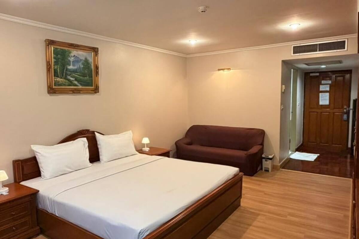 A bedroom with a wooden bed, a nightstand, a lamp, a painting on the wall, and a door leading to another room.
