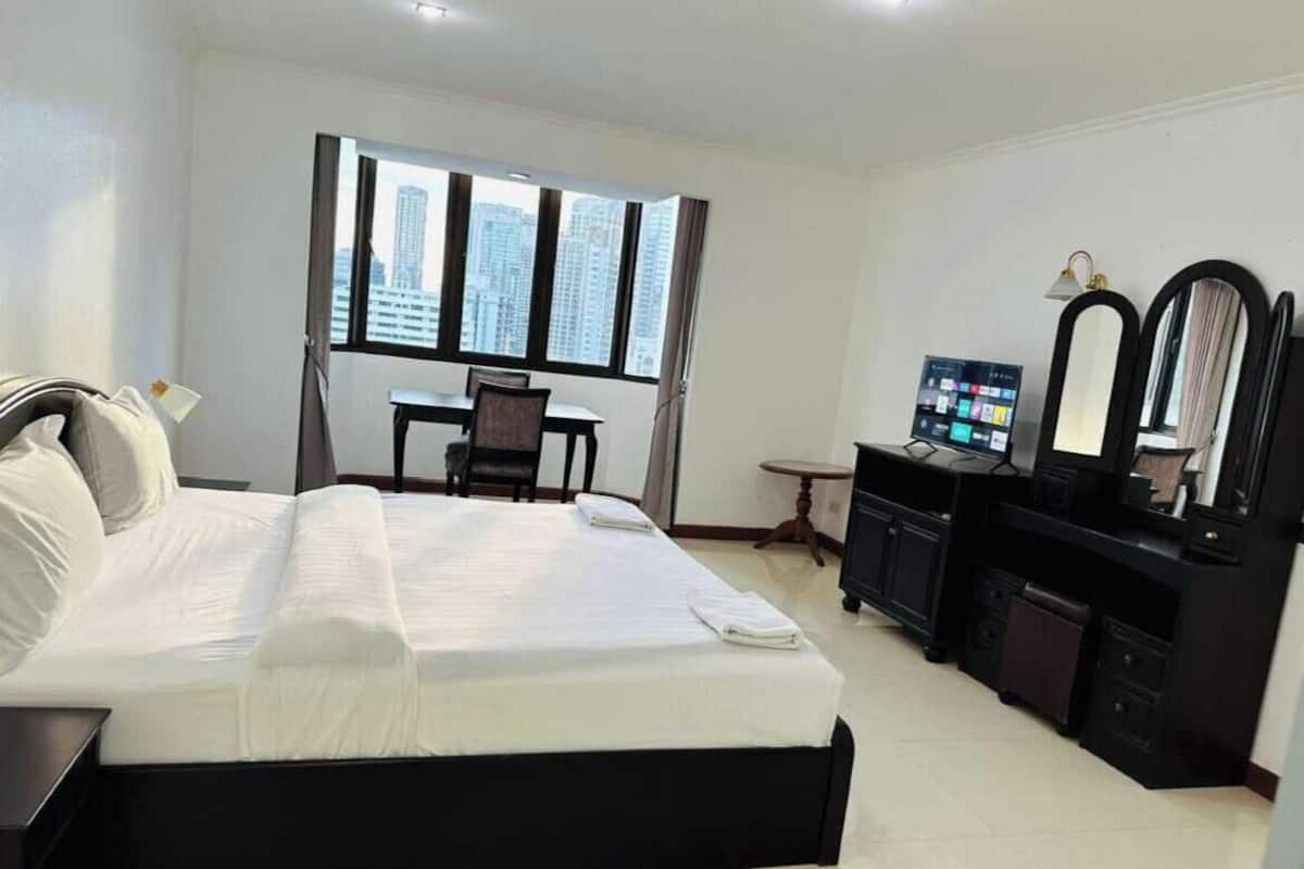 A hotel room with a bed, desk, computer, and large windows with a city view.
