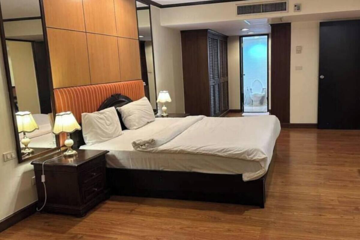 A hotel room with a bed, bedside tables, a dresser, a TV, and a door leading to a balcony.