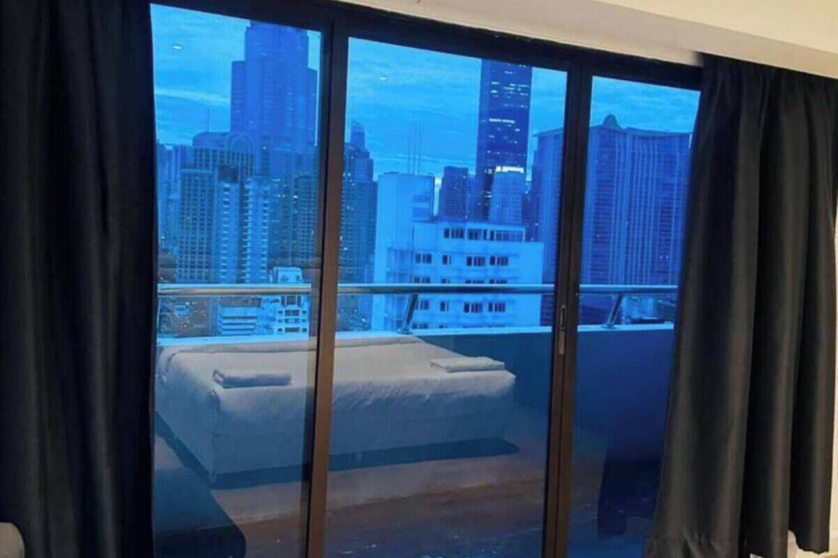 A room with a bed, a sofa, and a view of a cityscape through large windows.