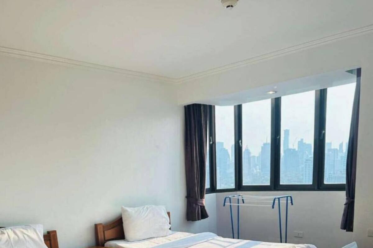 A hotel room with two beds, a view of the city through large windows, and a wooden floor.