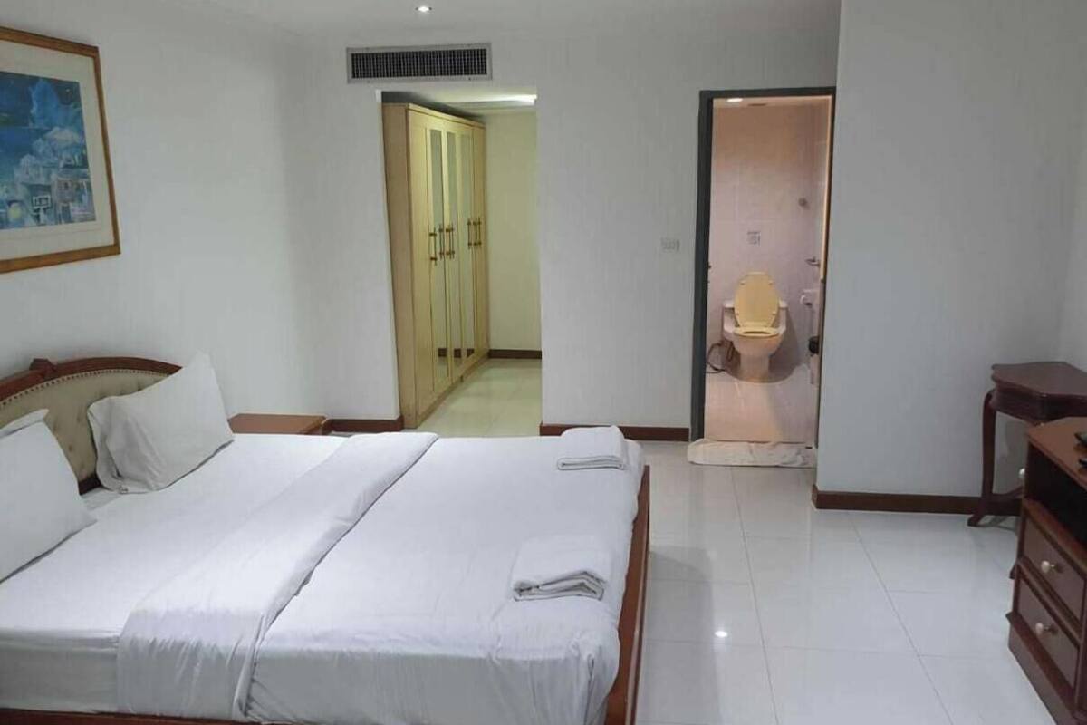 A hotel room with a bed, a wooden dresser, a toilet, and a door leading to a hallway.