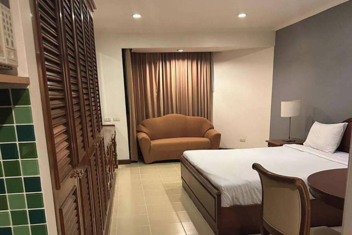 A compact hotel room with a bed, a small sofa, a dining table with chairs, and a window with curtains.