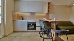 A compact kitchen with a dishwasher, oven, and a dining area with a green sofa and two chairs. - Villa Betina - Apartman Ambienta by Villas Guide (Lovran)