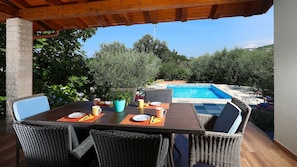 An outdoor dining area with wicker furniture, a pool, and surrounding greenery. - Villa Kostrena in a green oasis by Villas Guide (Kostrena)