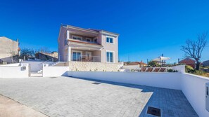 A modern two-story house with a balcony, a paved driveway, and a clear blue sky.