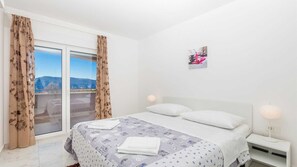 A bedroom with a bed, two pillows, a nightstand with a lamp, and a window with curtains.