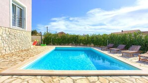 Une piscine rectangulaire bordée de pierres, entourée d’un mur de pierres et d’une rangée de chaises longues.