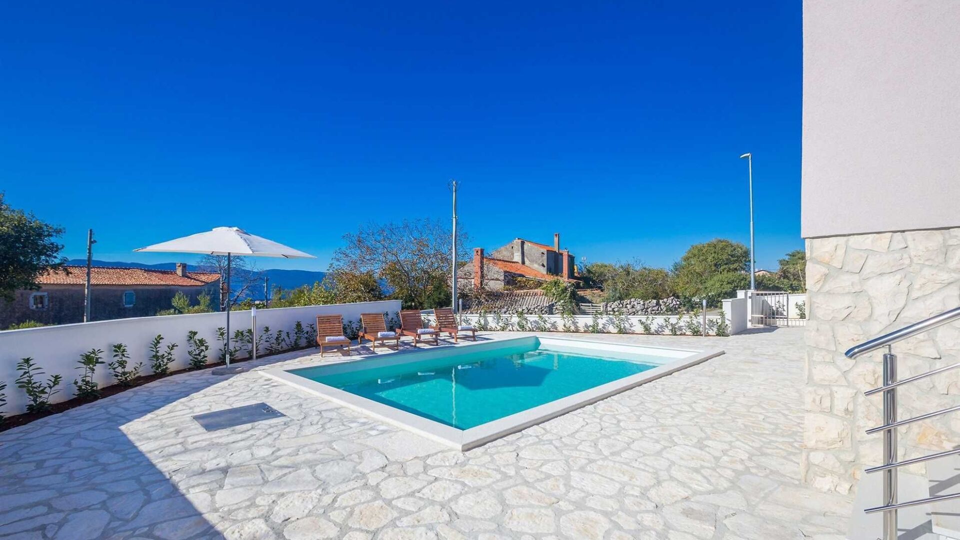 A swimming pool with stone flooring, two lounge chairs, and a white umbrella.