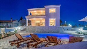 A modern two-story house with a swimming pool, outdoor furniture, and a stone facade.