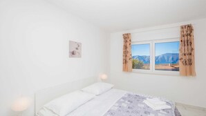 Une chambre à coucher avec un lit, deux lampes de chevet, une fenêtre avec des rideaux et un tableau accroché au mur.