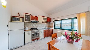 Eine kleine Küche mit Meerblick, einem Esstisch mit Stühlen und einem Kühlschrank.