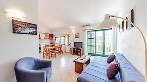 Ein Wohnzimmer mit Sofa, Sessel, Fernseher und Essbereich mit Tisch und Stühlen.