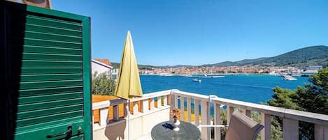 A balcony with a table and chairs, overlooking a coastal town with boats and a clear blue sky.