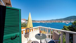 Ein Balkon mit Tisch und Stühlen, mit Blick auf eine Küstenstadt, Boote und einen strahlend blauen Himmel.