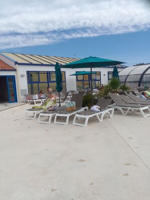 Een zwembadgedeelte met ligbedden, parasols en een gebouw met grote ramen.