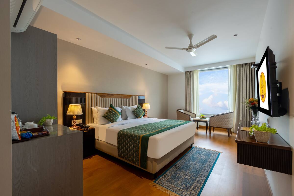 Ein Hotelzimmer mit einem großen Bett, einem Schreibtisch, einem Sessel, einem Fernseher und Blick zum Himmel.
