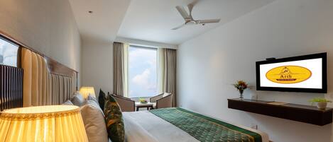 A hotel room with a bed, a desk, a television, and a ceiling fan.