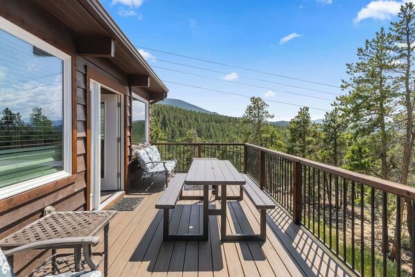 A wooden deck with a picnic table and chairs, overlooking a forested area.
