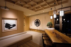A modern interior with a wooden dining table, a bench, a projector, and a decorative wall piece. - Blossom House Shibuya (Shibuyakumaruyamacho)