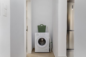 A laundry room with a washing machine, a green basket, and a folding chair.