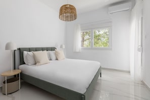 A modern bedroom with a bed, bedside tables, a window, and an air conditioning unit.
