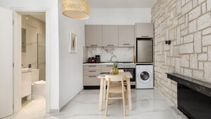 A modern kitchen with a stone wall, a dining area with a table and chairs, and a washing machine. - Glow Apartments (Perea)