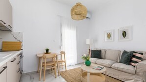 A modern kitchen with white cabinets, a wooden dining table, and a round coffee table with a magazine. - Glow Apartments (Perea)