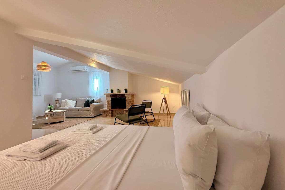 A bedroom with a bed, a sofa, a fireplace, and a lamp.