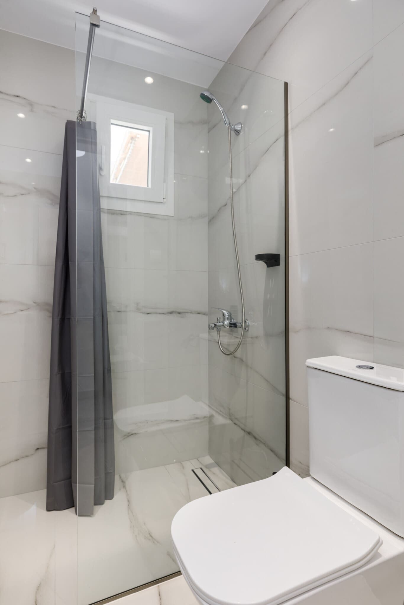Un baño moderno con ducha de vidrio, inodoro blanco y paredes de mármol.