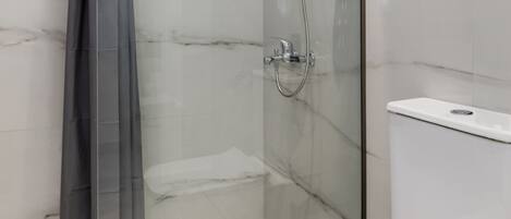 Un baño moderno con ducha de vidrio, inodoro blanco y paredes de mármol.