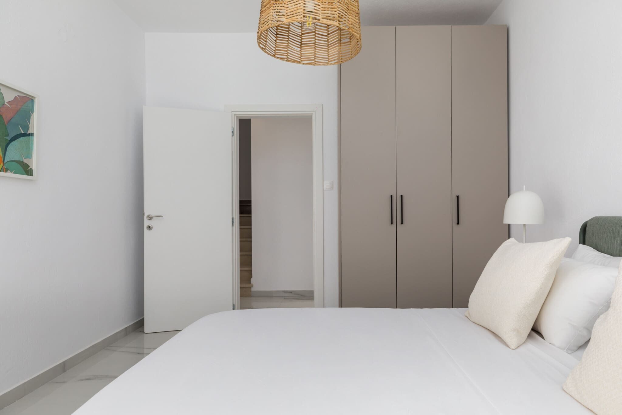 A bedroom with a bed, a wardrobe, a door leading to a hallway, and a hanging light fixture.