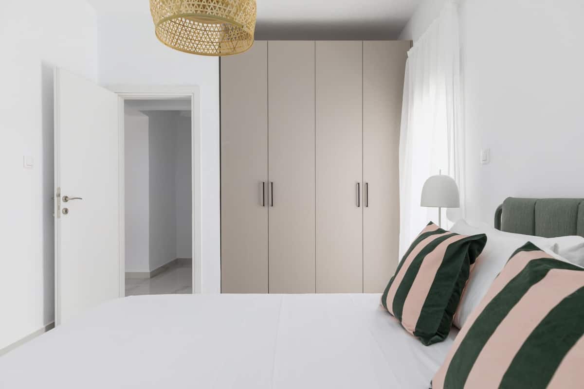 A bedroom with a bed, a wardrobe, a door, and a hanging light fixture.