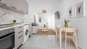 A modern kitchen with a built-in oven, a washing machine, and a dining area with a table and chairs. - Glow Apartments (Perea)