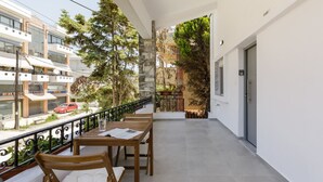 A balcony with a table and chairs, a railing, and a view of the street and buildings. - Glow Apartments (Perea)