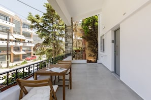 A balcony with a table and chairs, a railing, and a view of the street and buildings.