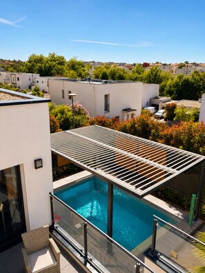 A rooftop pool with a pergola, surrounded by modern buildings and greenery.