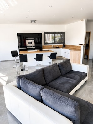 A modern living room with a sofa, a kitchen area with a microwave, and a bar area with chairs.