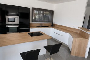 A modern kitchen with black appliances, a wooden countertop, and two black chairs.