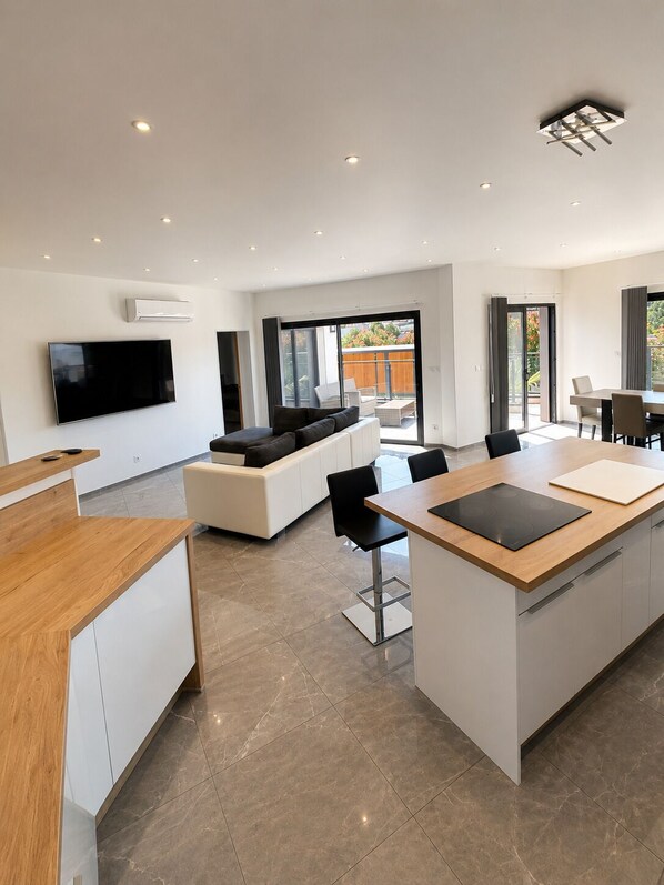 A modern kitchen with a central island, built-in appliances, and a flat-screen TV mounted on the wall.