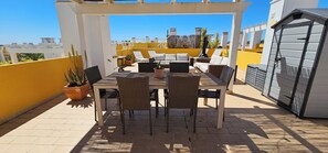 Un patio esterno coperto con tavolo e sedie, piante in vaso e un barbecue.