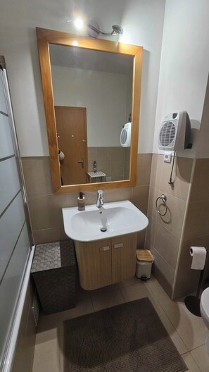 Un bagno con un mobile bagno in legno, un lavabo, uno specchio, un portascopevoli, un water e un'area doccia.