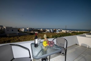 A table with a bottle of wine, glasses, and fruit on a balcony overlooking a coastal cityscape. - THE F SUITES (KARTERADOS)