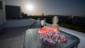 A table with a bottle of wine, a pineapple, and a watermelon on a balcony with a cityscape view. - THE F SUITES (KARTERADOS)