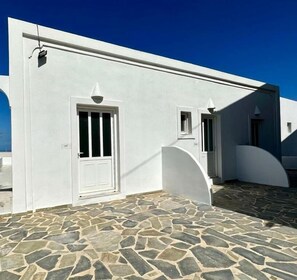 Un edificio blanco con un patio empedrado de piedra, una puerta y una pequeña ventana.