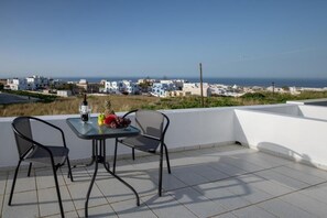Une terrasse avec une table et des chaises, d’où l’on a une vue sur une ville côtière aux bâtiments blancs et sur la mer.