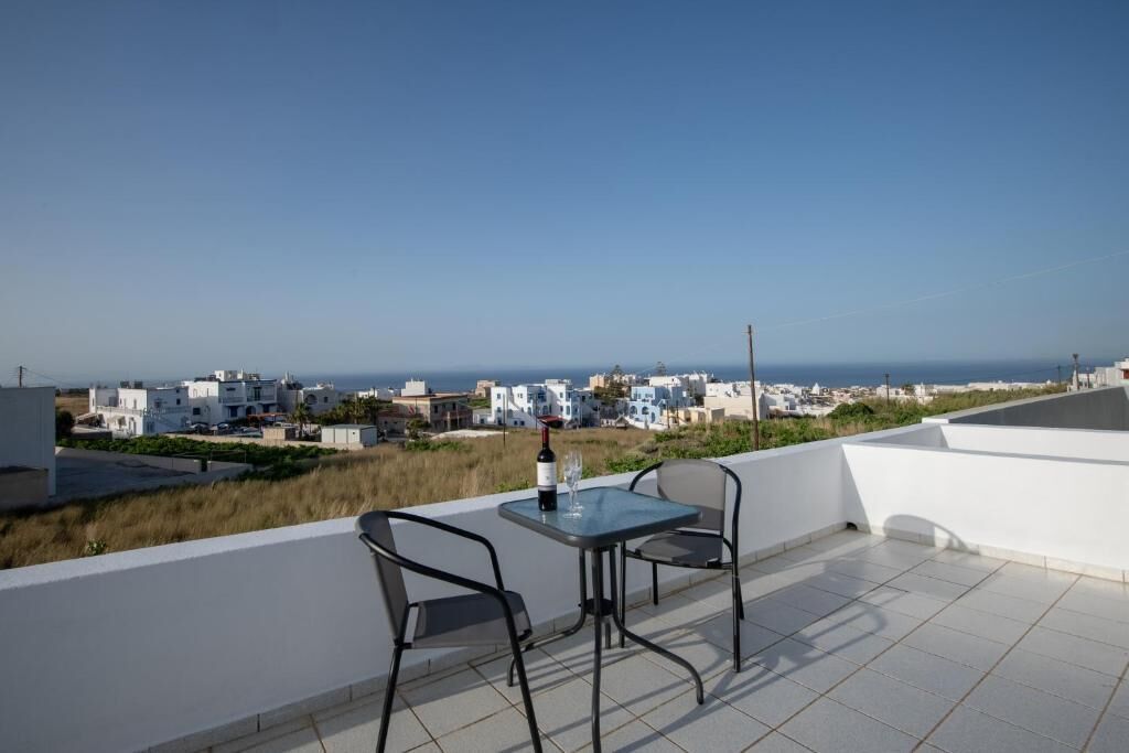 A terrace with a table and chairs, a bottle of wine, and a view of the sea and buildings.