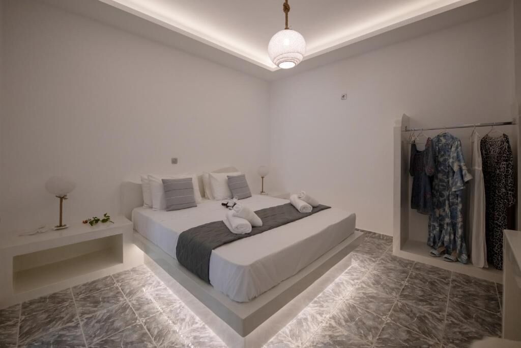 A modern bedroom with a bed, bedside tables, a hanging light fixture, and a clothing rack.
